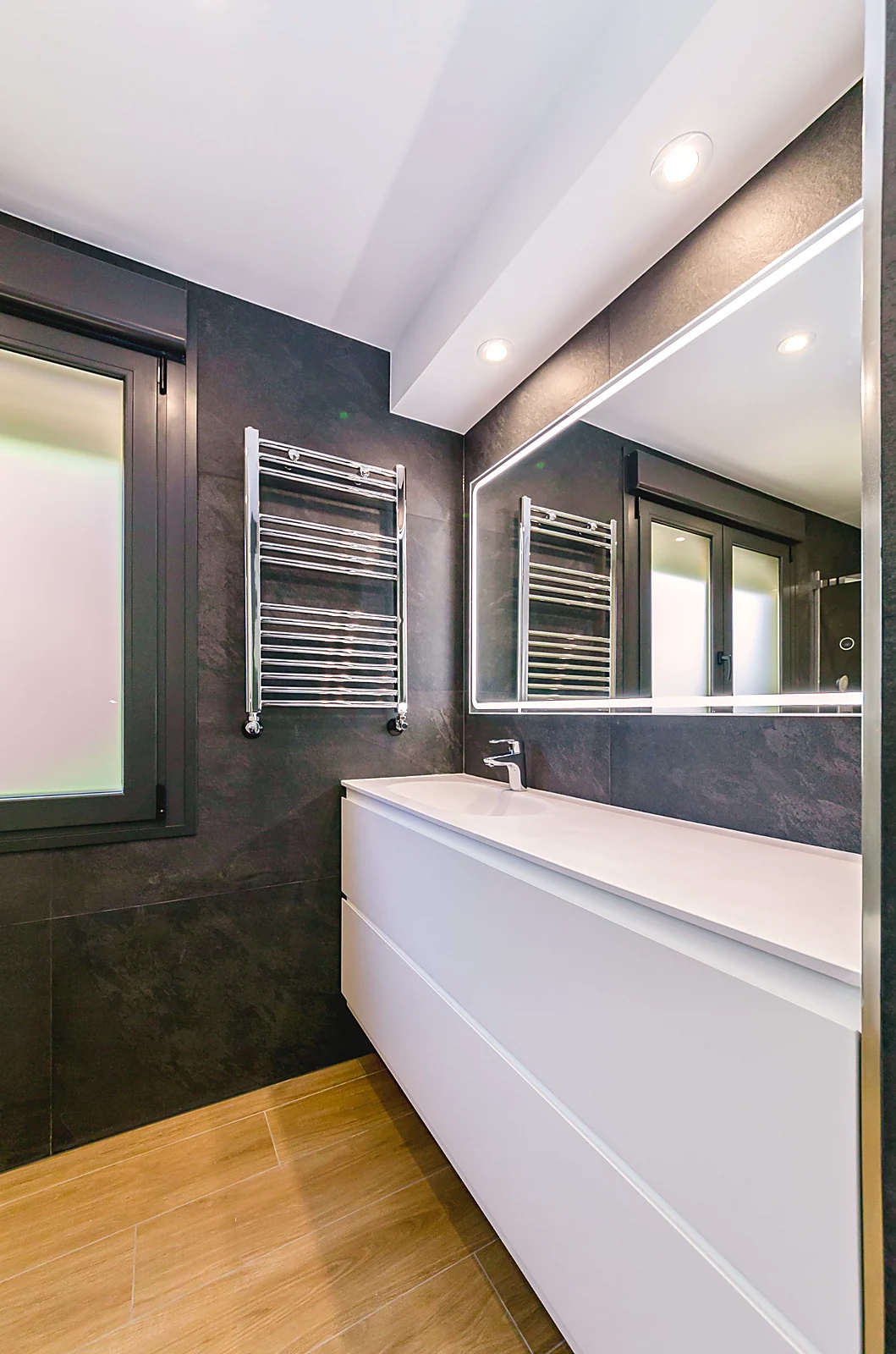 Baño oscuro con lavabo blanco y espejo iluminado.. Fotografía 1
